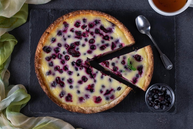 Homemade open blackcurrant shortbread pie on a slate plate on a dark background top view