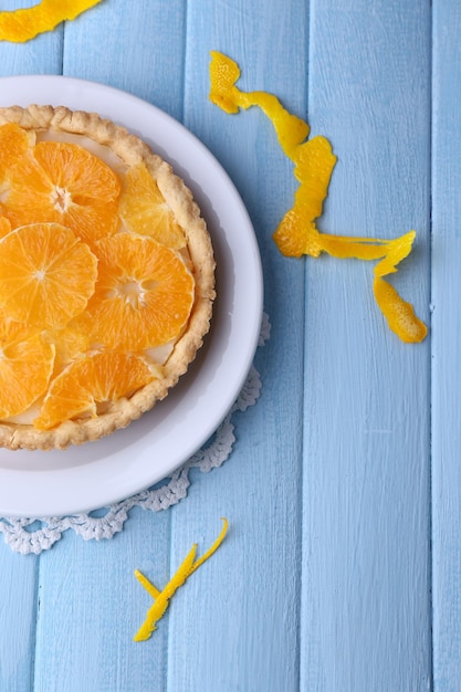 Homemade orange tart on plate on color wooden background