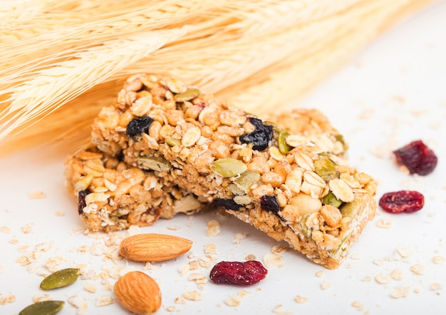 Homemade organic granola cereal bar with nuts and dried fruit on white with oats and raw wheat.