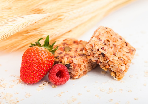 Homemade organic granola cereal bars with nuts and dried fruit on white with oats and raw wheat and strawberry