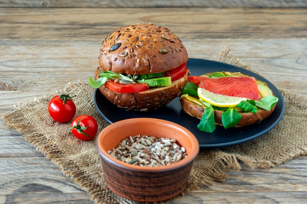 Hamburger di salmone biologico fatto in casa con pomodoro, insalata di mais e avogado su un piatto su sfondo di legno. cibo biologico sano.