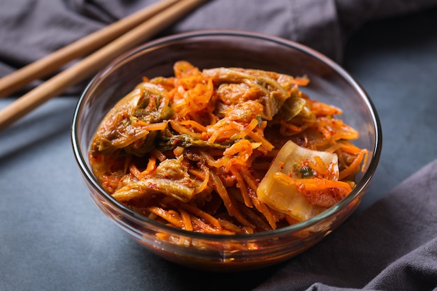 Homemade organic traditional korean kimchi cabbage salad with chopsticks on a dark table. Fermented vegetarian, vegan preserved gut health food concept