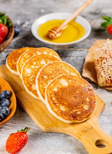 Homemade pancakes on a cutting board with honey and berries