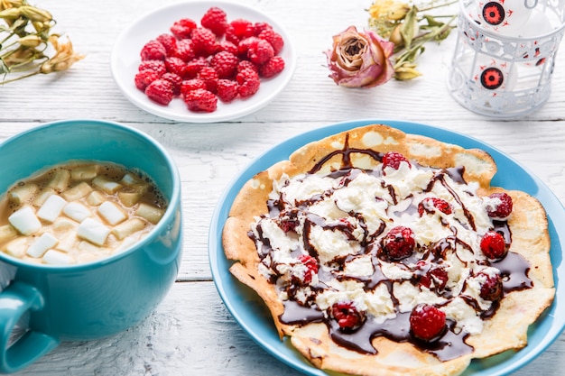 Homemade pancakes or Russian pancakes with chocolate sauce, whipped cream and raspberries 