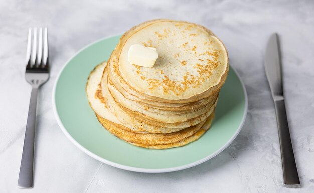 Homemade pancakes stacked with butter on a green plate and cutlery Selective focus
