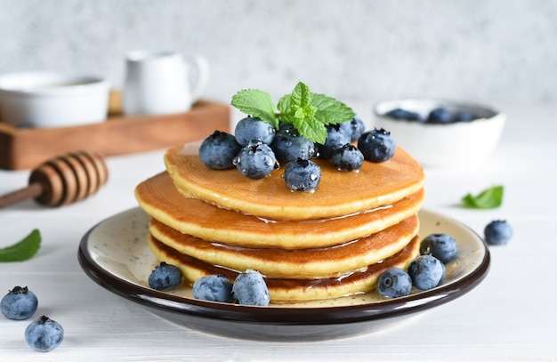 Homemade pancakes on a white plate with honey and blueberries for breakfast. Good morning!