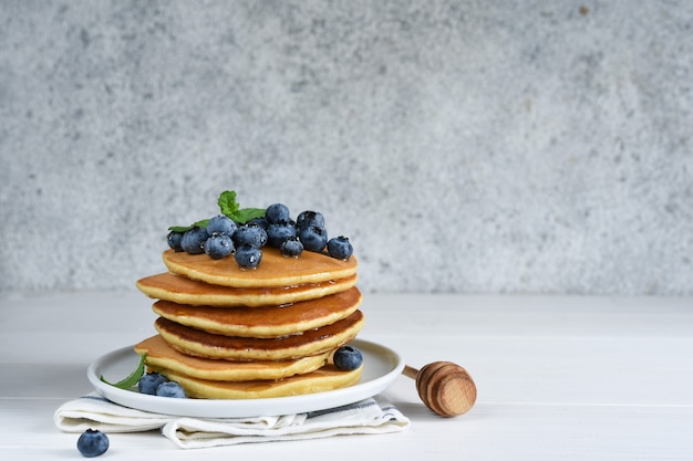 Homemade pancakes on a white plate with honey and blueberries for breakfast. Good morning!