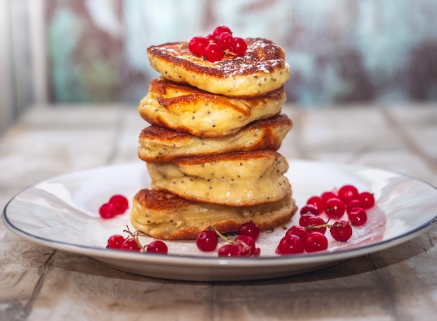 Homemade pancakes with currant berries are stacked in a high stack on a white teatka closeup