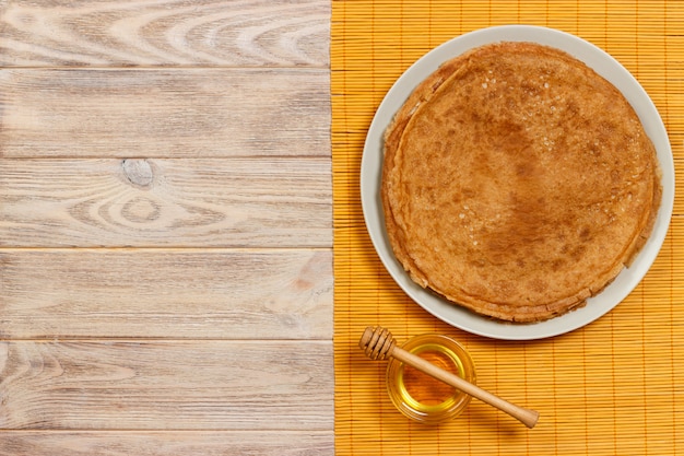 Homemade pancakes with honey on white plate, dipper, wooden table. top view. copy space