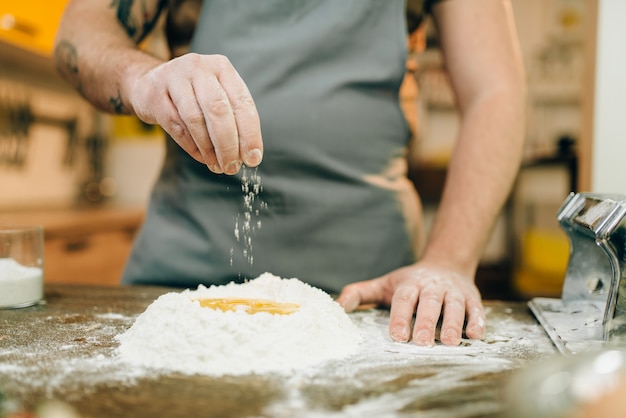 Homemade pasta cooking, man preparing dough. Egg and bunch of flour on wooden table