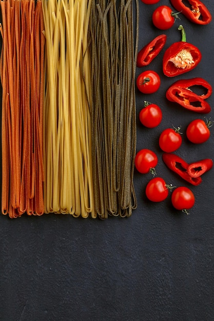 Homemade pasta noodles in different colors with natural vegetable ingredients on a black concrete table