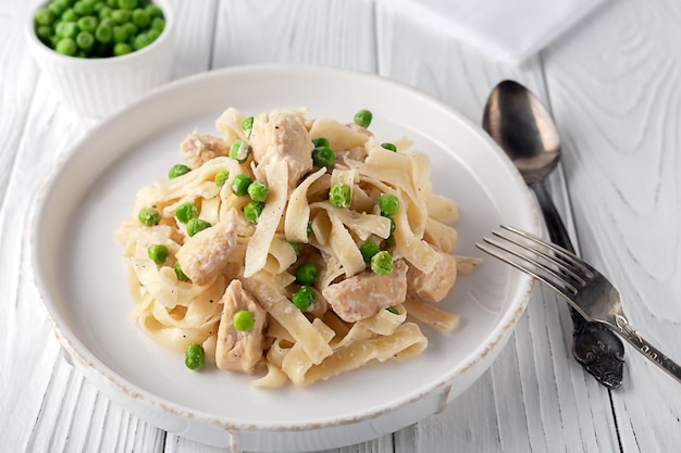Homemade pasta with green peas chicken and cream sauce on a white wooden background on a white woode...