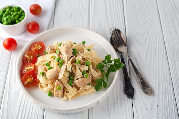 Homemade pasta with green peas, chicken and cream sauce on a white wooden background on a white wooden background