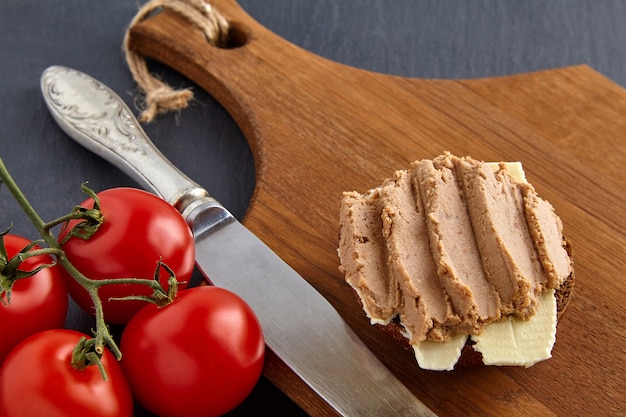 Homemade pate sandwich on wooden board on stone black table with cherry tomatoes and kitchen knife