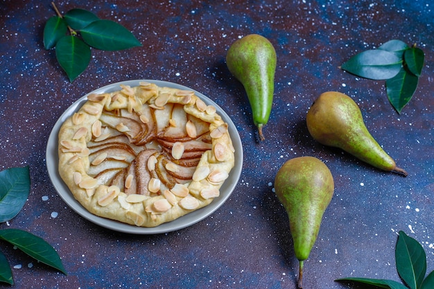 Homemade pear galette pie with almond leaves and fresh ripe green pears