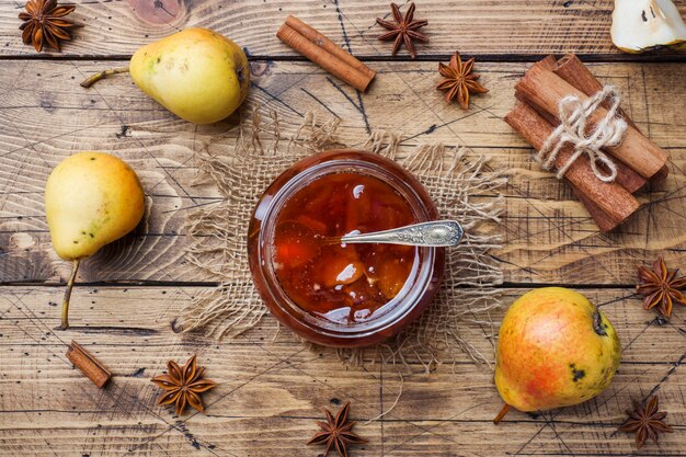 Homemade pear jam in a jar and fresh pears on a wooden background.