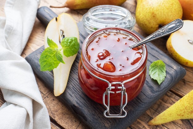 Homemade pear jam in a jar and fresh pears on a wooden background.