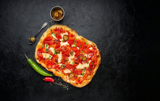 Homemade pepperoni square pizza or pinza with melted mozzarella cheese, fresh green onion and chilli pepper on black background, top view, flat lay, copy space