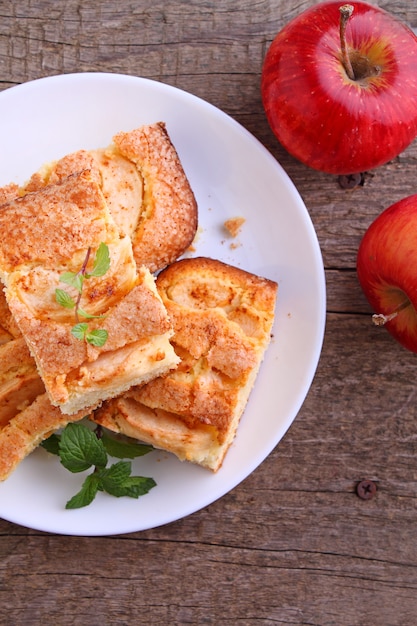 Homemade pie with apples and cinnamon is cut slices on a plate, wooden background