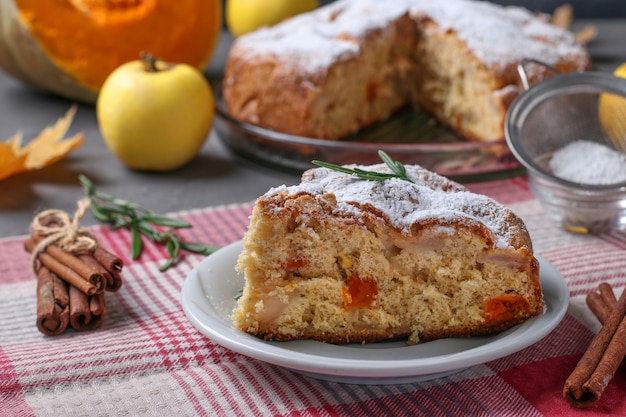 Домашний пирог с яблоками и тыквой, посыпанный сахарной пудрой на белой тарелке.