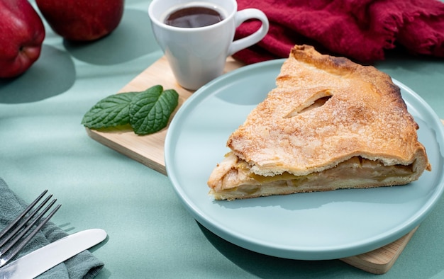 Homemade piece of apple pie with fresh red apples on green table