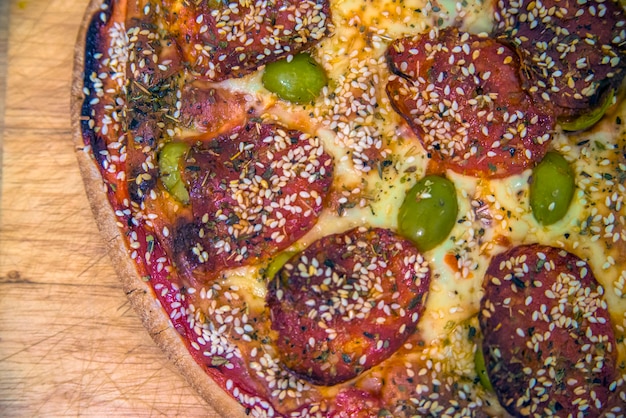 Photo homemade pizza on old wooden table, close up. fast food. mexican pizza with pepperoni, vegetables, cheese on wood table with copy space. top view