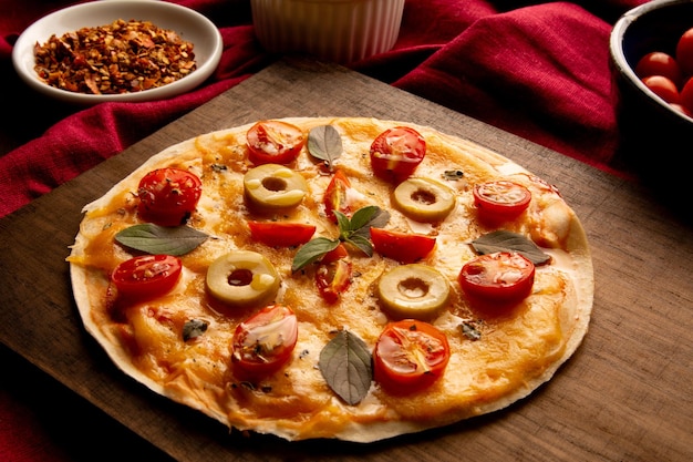 Homemade Pizza pan with tomatoes basil and olives in a wooden plate in top view