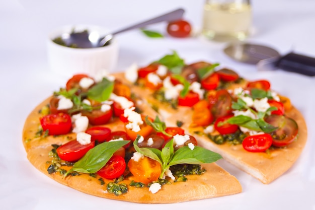 Homemade pizza with cherry tomatoes, fresh green basil and feta cheese. Homemade food. Concept for a tasty and hearty meal. Wooden surface. Close up.