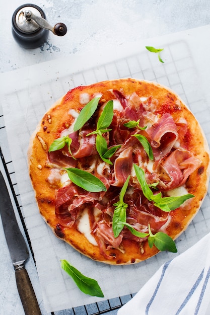 Homemade pizza with jamon, mozzarella and basil leaves on concrete old background. Top view.