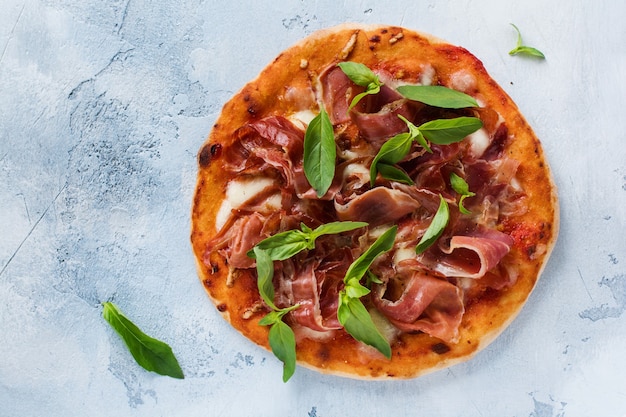 Homemade pizza with jamon, mozzarella and fresh basil leaves  