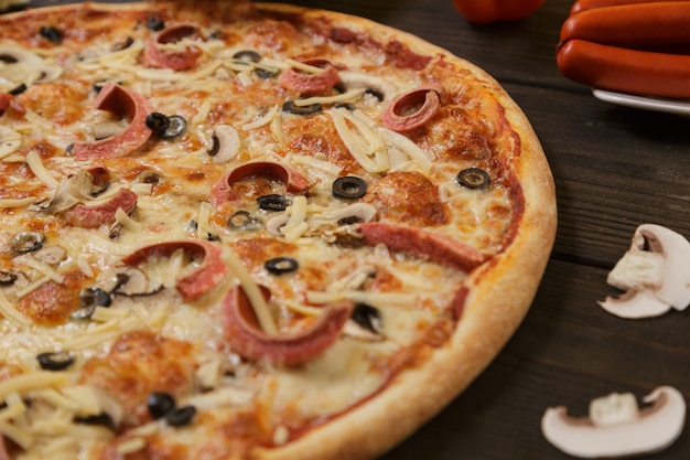 Homemade pizza with pepperoni sausage and mushrooms on a wooden table with ingridients