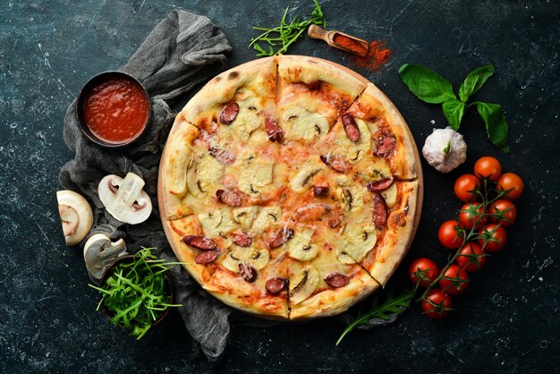 Homemade Pizza with sausages, mushrooms and cheese. On a black stone background. Free space for text.