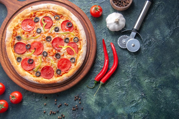 Homemade pizza on wooden cutting board and pepper garlic tomatoes on isolated dark surface in close up shot