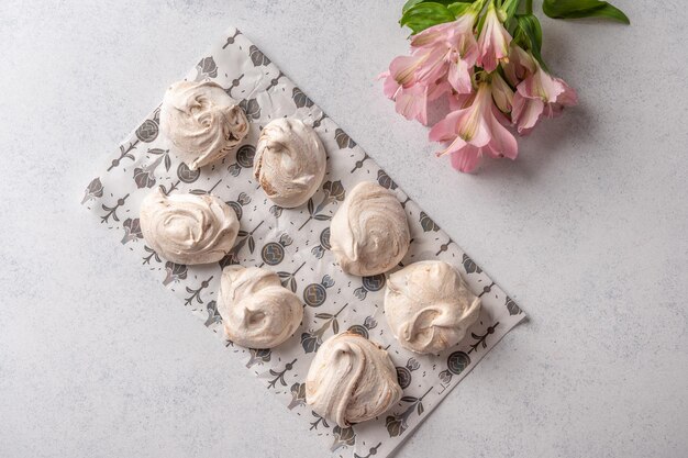 Homemade popular eggs dessert meringue on a pastry paper on light background next to pink flower top