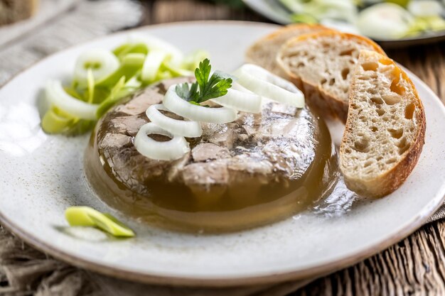 Foto jelly di carne di maiale aspico fatto in casa con cipolla e porro in un piatto bianco