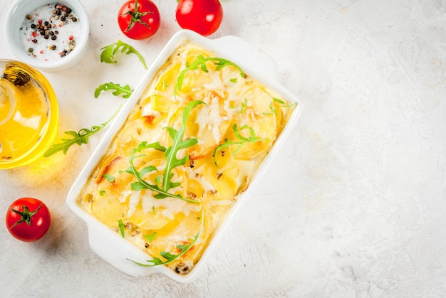 Homemade potato gratin in a ceramic frying pan on a white marble stone