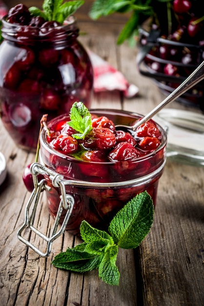 Marmellata di amarene e menta conservata casalinga, con le ciliege fresche sullo spazio di legno vecchio rustico della copia del fondo