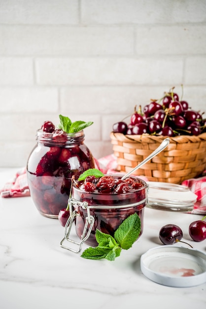 Homemade preserved cherry and mint jam, with fresh cherries on white marble background copy space