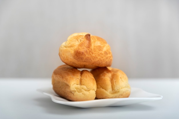 Homemade profiteroles or eclairs without cream on saucer. Gray background.