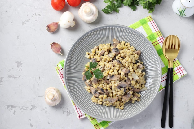 Homemade ptitim pasta with champignons in a plate on light gray table Horizontal format Top view