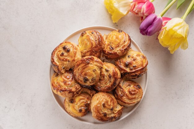 Homemade puff buns with custard cream and raisins in a ceramic plate on a light surface