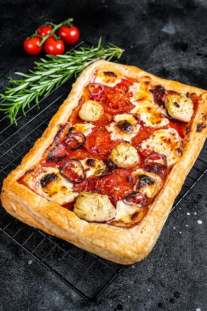 Homemade puff pastry pizza with salami mozzarella tomatoes and cheese Black background Top view