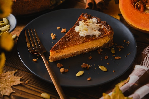 Homemade pumpkin cheesecake decorated with whipped cream on black plate made for Thanksgiving. The toning. selective focus