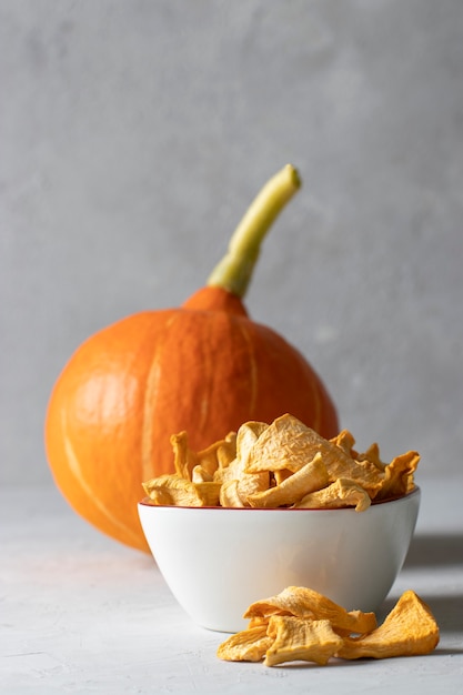 Homemade pumpkin chips in a white bowl on a light gray background.