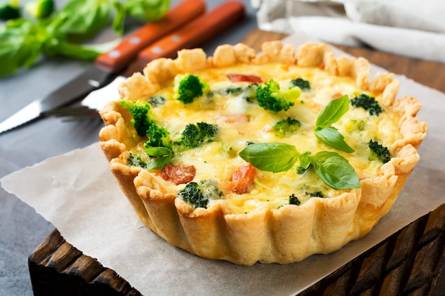 Homemade quiche tart with red fish salmon, broccoli, basil, seasonings and cheese on a gray stone table. Selective focus.