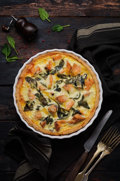 Homemade quiche tart with red fish and spinach on dark wooden surface