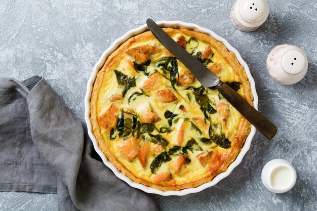 Homemade quiche tart with red fish and spinach on light wooden surface