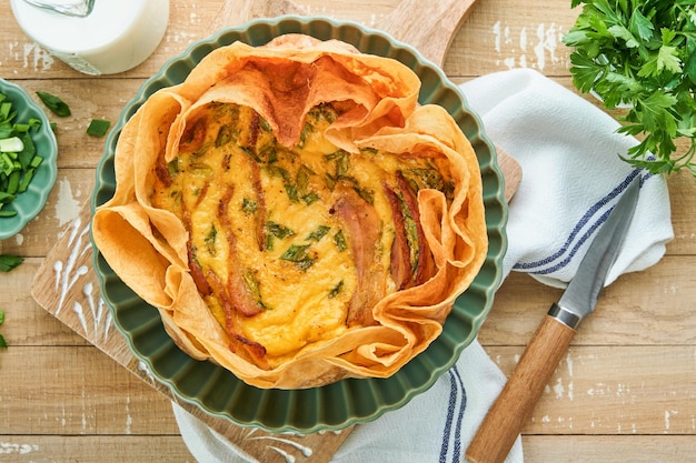 Homemade quiche or tart with slices of bacon and leeks with tortilla instead of dough on wooden cutting board on rustic old wooden background Quiche open tart traditional French cuisine Top view