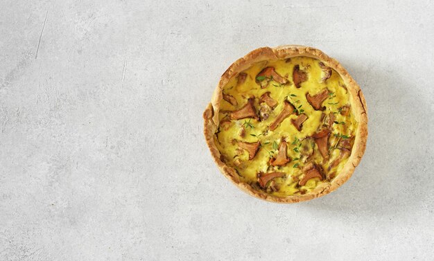 Homemade quiche with chanterelle mushrooms on light background top view copy space