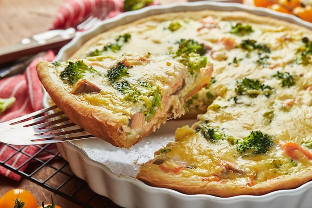 Homemade quiche with red fish, salmon, broccoli and cheese on wooden background